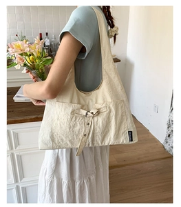 Détail du sac cabas en toile crème montrant les grandes poches avant et l'étiquette logo