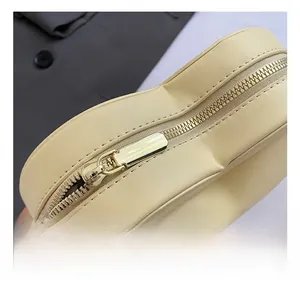Detailed close-up of light gold zipper closure on beige heart-shaped crossbody bag