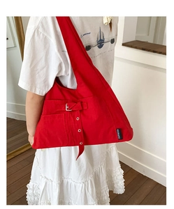 Détail d'un grand sac cabas en toile rouge avec boucle argentée et étiquette latérale