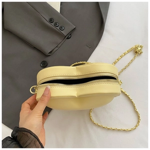 Detail of yellow heart-shaped crossbody bag featuring golden zipper and bear charm
