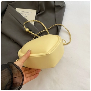 Detailed view of cream heart-shaped crossbody bag with gold chain strap on grey blazer