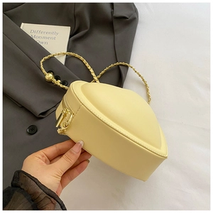 Detail of light yellow heart-shaped crossbody bag with golden zipper and leather chain strap