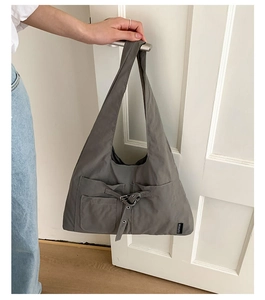 Détail du sac hobo en nylon gris avec poches cargo accroché à une poignée de porte