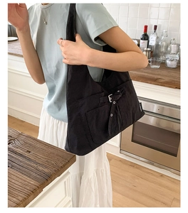 Détail d'un grand sac en toile noir avec poche avant et boucle métallique porté à l'épaule