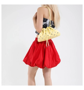 Detail of yellow patent leather bag featuring silver metal rivets and drawstring closure