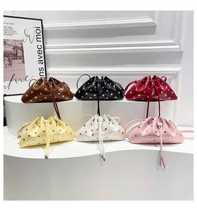 Detail showing various colors of studded drawstring bucket bags on a white tiered stand