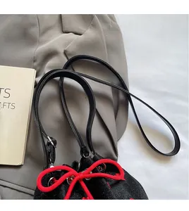 Detail of black canvas bucket bag with vibrant red drawstring bow and thin shoulder strap