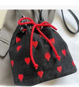 Close-up of black sparkly drawstring bucket bag with embroidered red hearts and leather strap