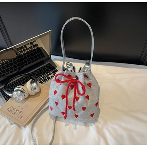 Silver bucket bag with red heart embroidery and drawstring closure on a desk