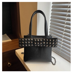 Detail of black pebbled leather handbag featuring a large studded bow and chain strap