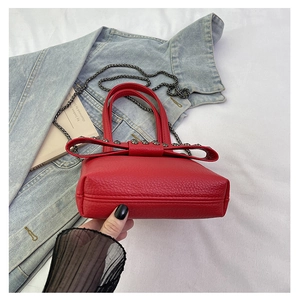 Detail of red leather mini bag with rivet bow knot on blue denim jacket backdrop