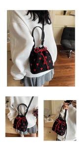 Detail of black canvas bucket bag featuring red heart embroidery and drawstring closure