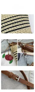 Detail of straw woven crossbody bag featuring red cherry charm and brown leather straps