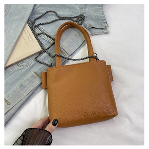 Detailed view of a brown pebbled leather mini tote bag with silver chain strap on denim fabric