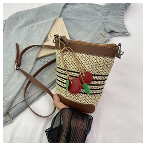 Detailed close-up of woven straw bucket bag with leather trim and cherry charms