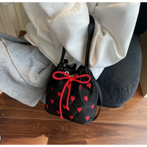 Detail of black drawstring bucket bag featuring red heart embroidery and silk bow