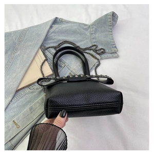 Detail of black lychee grain leather mini bag with rivet bow and metal chain strap
