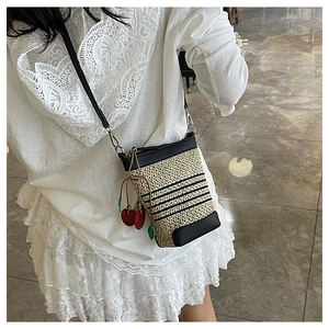 Detail of beige woven bucket bag with leather trim and decorative cherry charms