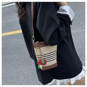 Detail of mini raffia bucket bag with leather trim and decorative red cherry charm