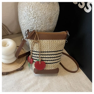Detail of straw woven bucket bag with leather trim and decorative cherry charms