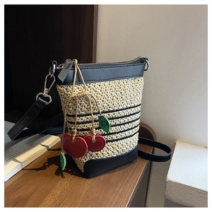 Detail of raffia bucket bag featuring black leather trim and cute red cherry charm