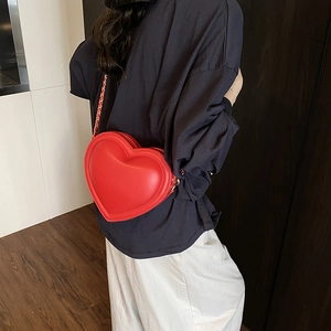 Minimalist red heart-shaped leather crossbody bag with woven chain strap on a model