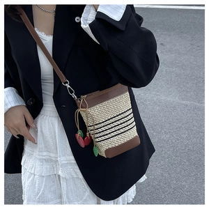 Detail of raffia woven crossbody bag featuring black stripes and cherry charm