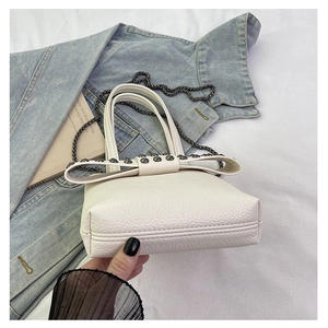 Close-up of white lychee leather phone bag featuring punk rivet bow and chain strap