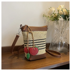Detail of woven straw handbag with brown leather trim and red cherry charm pendants