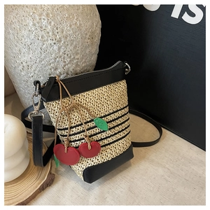 Detail of raffia woven crossbody bag with black stripes and decorative red cherry charms