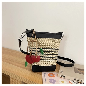Detail of woven raffia crossbody bag with black leather trim and red cherry charm accent
