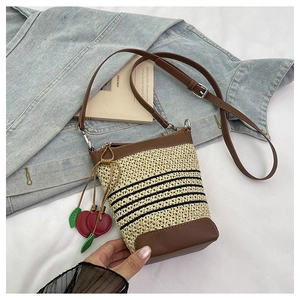 Detail of raffia bucket bag with black stripes, leather trim and cherry charm accessory