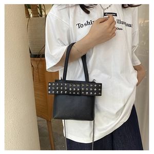 Detail of black pebbled leather crossbody bag with silver rivets and bow design
