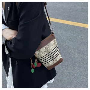 Detail of a woven rainbow bucket bag with leather trim and a cherry-shaped charm pendant