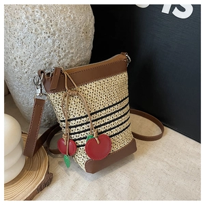 Detail view of woven raffia crossbody bag with leather trim and cherry charm accessory