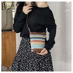 Detail of colorful striped woven crossbody bag with brown leather trim and metal zipper