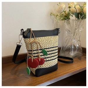 Detail view of woven straw bucket bag with black leather trim and cherry charm detail