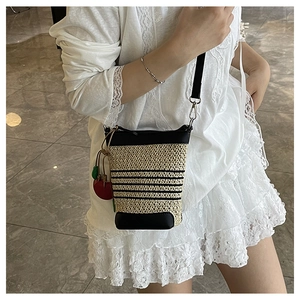 Close-up of straw bucket bag featuring black stripes and a cute red cherry charm detail