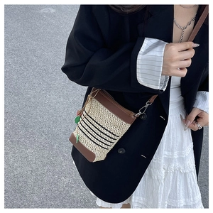 Detail of raffia crossbody bag with black stripes and green leaf charm on model