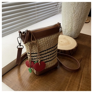 Detail of raffia woven crossbody bag with black stripes and cherry charm on wood base