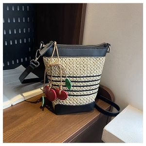 Close-up of beige raffia bucket bag with black leather trim and cherry charm on wood table