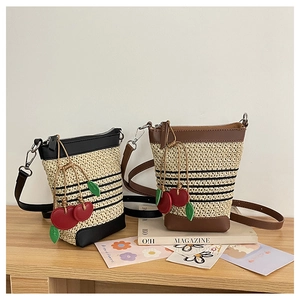 Detail of woven straw bucket bag with red cherry charm and leather strap detailing