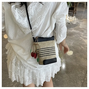Detail of woven raffia crossbody bag with black stripes and red cherry charm accessory
