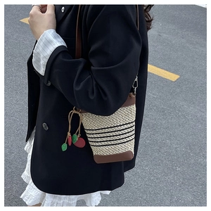 Detail of straw bucket bag with dark brown leather trim and cherry tassel ornament