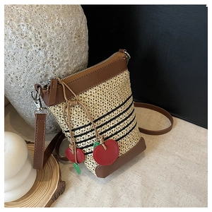 Close-up of raffia woven crossbody bag with black stripes and red cherry charm details