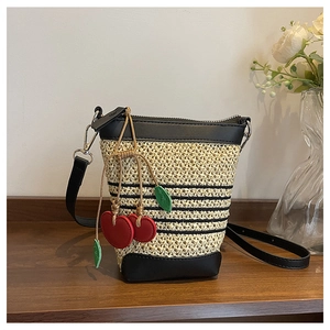 Detail view of woven raffia bucket bag with black leather trim and red cherry charm accent