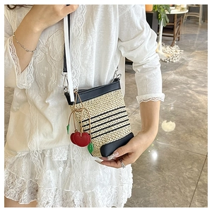 Detail of a straw crossbody bucket bag with black leather trim and cherry charm