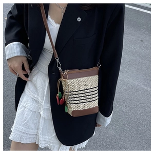 Detail of raffia woven crossbody bag featuring brown leather trim and cherry pendant