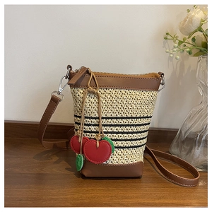 Detail of raffia straw crossbody bag with brown leather trim and red heart charm