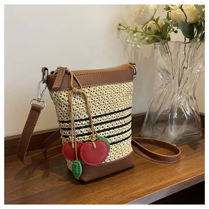 Detail of raffia woven crossbody bag with brown leather trim and red cherry charm